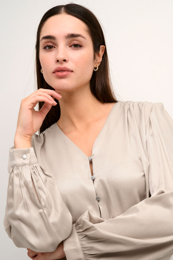 A simple silky feel blouse in a beautiful Oyster colour from Danish brand Kaffe. The official colour is Feather grey however it is more of a creamy oyster colour. It has a flattering V neck with 3 pretty silver coloured metallic buttons . The long sleeves have a single button on the cuff. There is slight gathering on the shoulders. The fit is true to size.